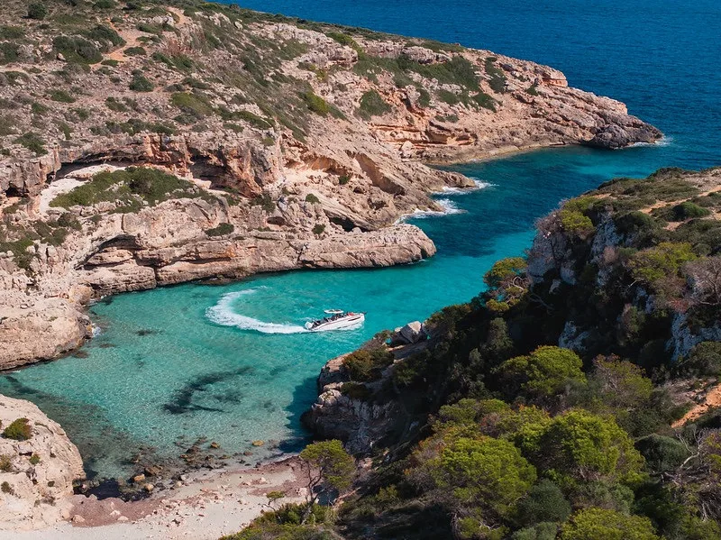 The NAVAN S30 anchored alone in a secluded turquoise cove framed by ochre cliffs on Ibiza