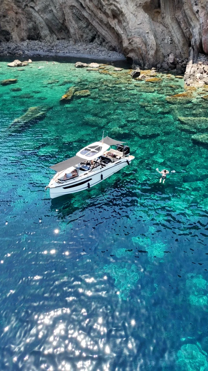 Guest swimming next to the anchored NAVAN S30 beneath tall cliffs in a quiet Ibiza cove