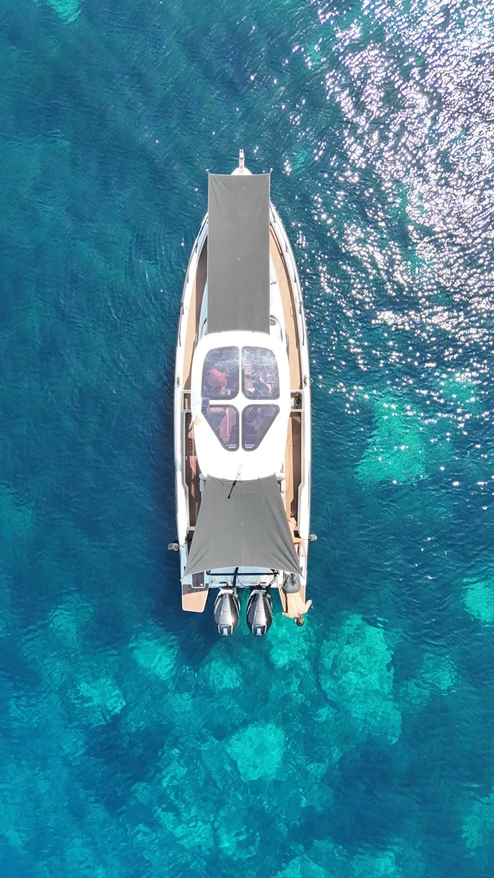 Vista aérea del NAVAN S30 fondeado sobre aguas turquesas cristalinas en Ibiza, con toldos de sombra en proa y popa