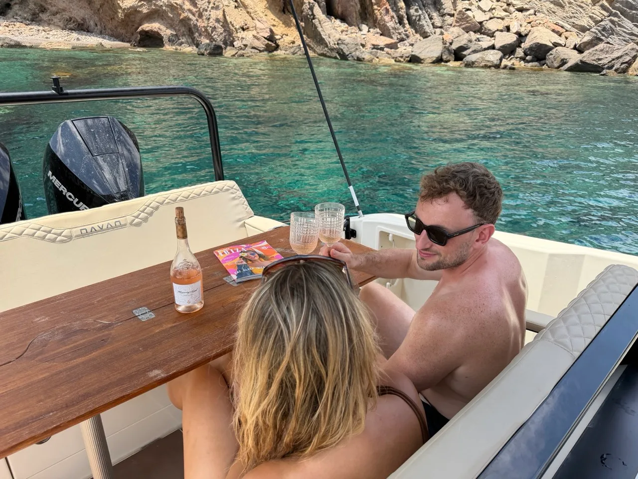 Zwei Gäste entspannen mit einem Glas Rosé am Teaktisch der NAVAN S30 in einer ruhigen Bucht