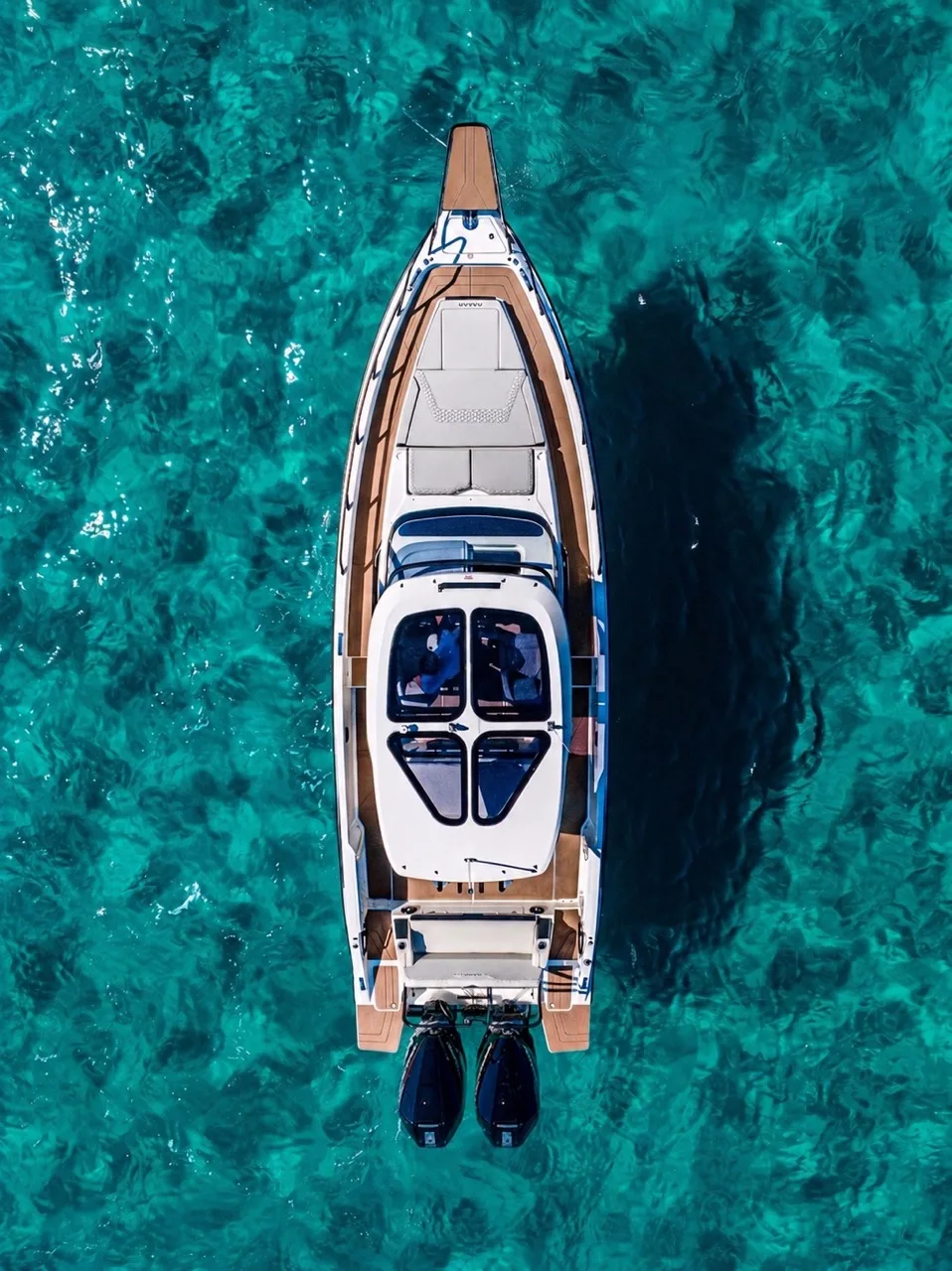 Aerial view of the Balearic Waves NAVAN S30 on turquoise water, showing the full deck layout with sunpads, T-top and twin outboard engines