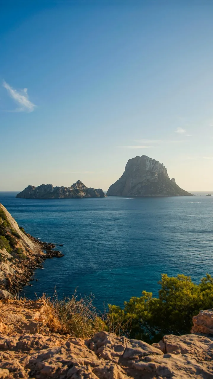 Es Vedrà and Es Vedranell rising from a deep-blue Mediterranean, seen from the cliffs near Cala d'Hort