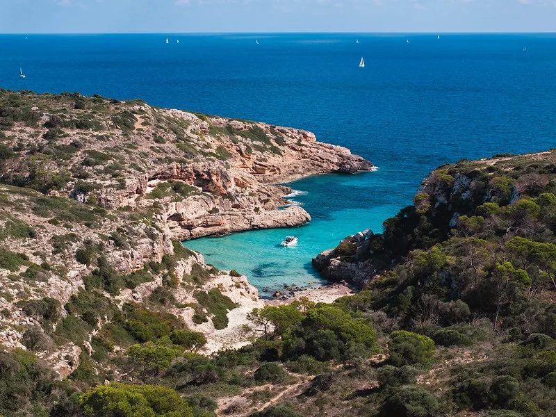 Die NAVAN S30 allein vor Anker in einer von Pinien gesäumten Bucht an Ibizas Küste, von den Klippen aus gesehen
