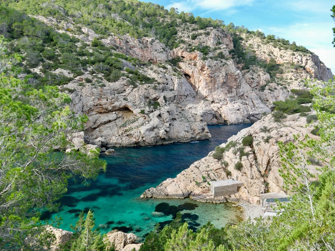 Tiny hidden cove on Ibiza's north coast with an old fisherman's hut above clear emerald water